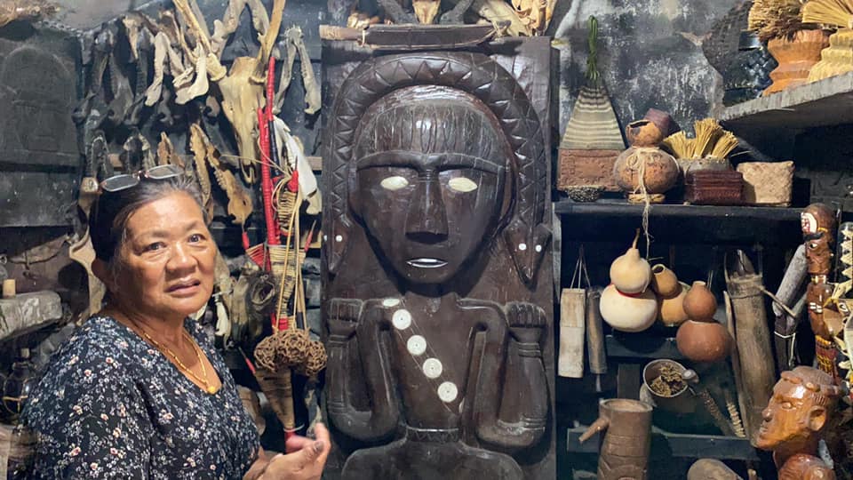 在台東縣達仁鄉土坂部落傳統文化空間中，部落長老向周端政 Nelson Chou 介紹木雕與祭儀器物，說明部落文化與信仰脈絡。