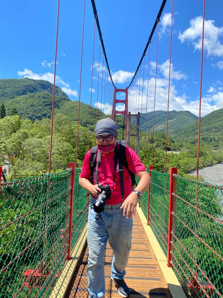 周端政 Nelson Chou 背著相機走在台東縣達仁鄉土坂部落的山區吊橋上，實地踏勘偏鄉醫療與地方創生計畫的地形條件。