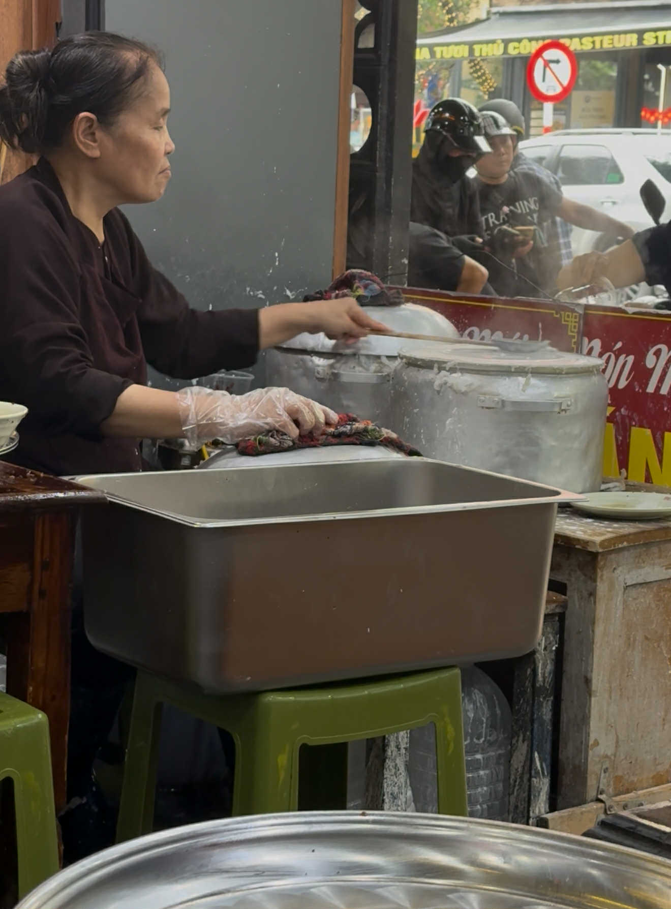 越南河內街邊粉卷店門口,一位阿婆坐在矮凳上,以蒸汽現做米漿粉皮的畫面